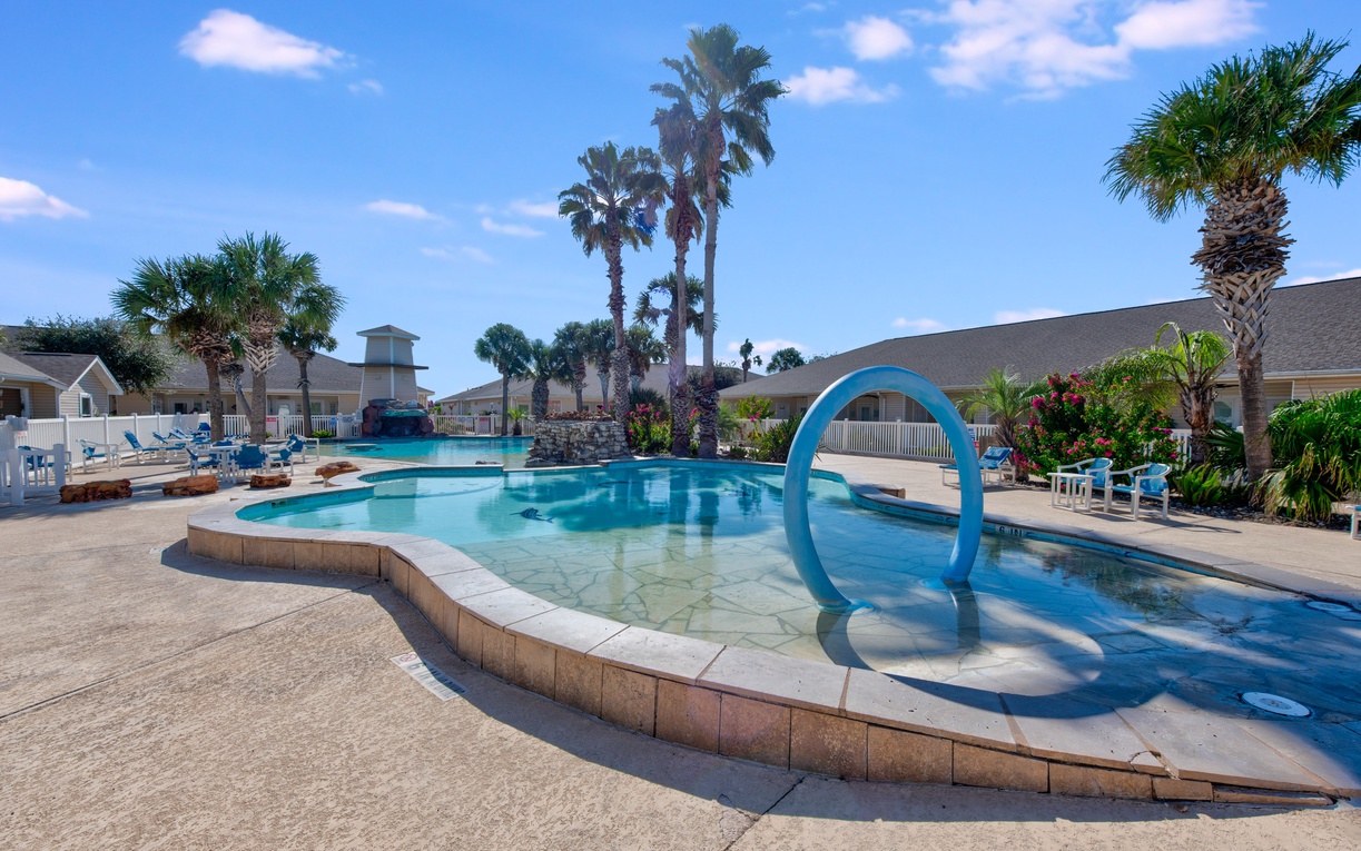 Resort-style pool with tropical palms and blue arch water feature creates a perfect vacation atmosphere under sunny skies.