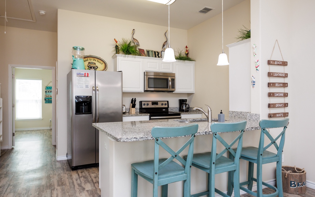 Your fully equipped kitchen features granite counters, stainless appliances, and coastal-themed seating perfect for morning coffee or casual meals.