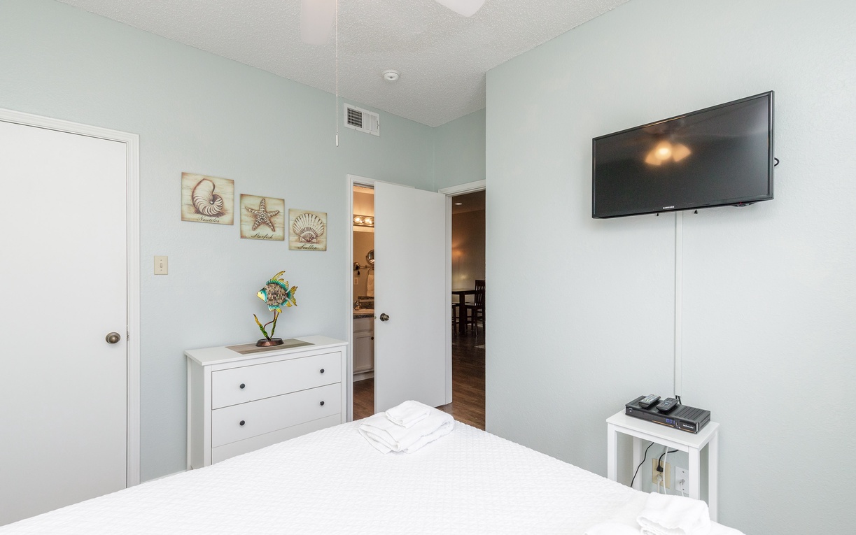 Relax in your peaceful bedroom with coastal artwork, modern TV, and soothing light blue walls that create a calming retreat.