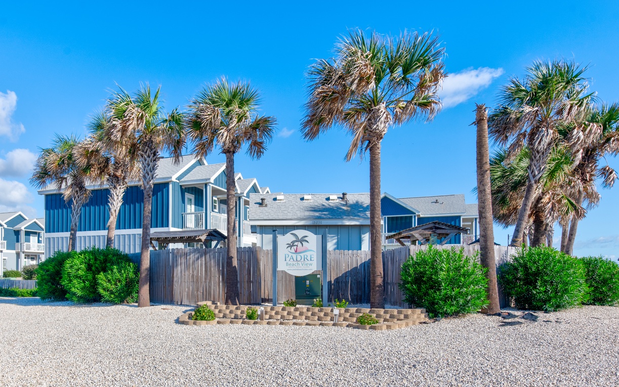 Coastal vacation rental property featuring blue beach house architecture surrounded by palm trees under clear blue skies.