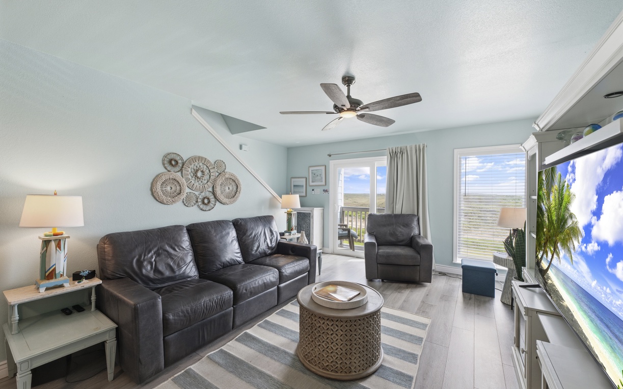 Unwind in this inviting space with leather seating, coastal decor, and distant views framed by sliding glass doors. Ceiling fan and natural light create a refreshing seaside retreat.