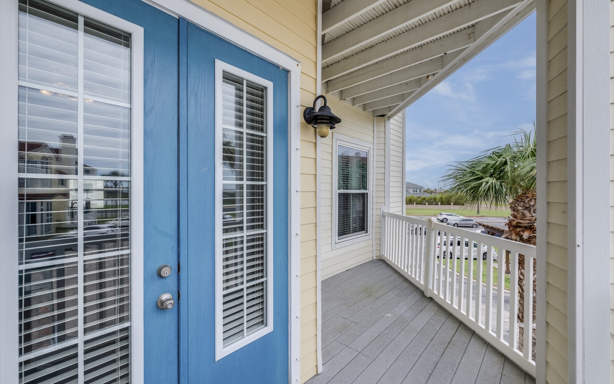 The property welcomes you with coastal charm—this inviting front porch features a charming blue door, nautical-style lighting, and views of palm-dotted surroundings. A perfect start to your beachside escape.