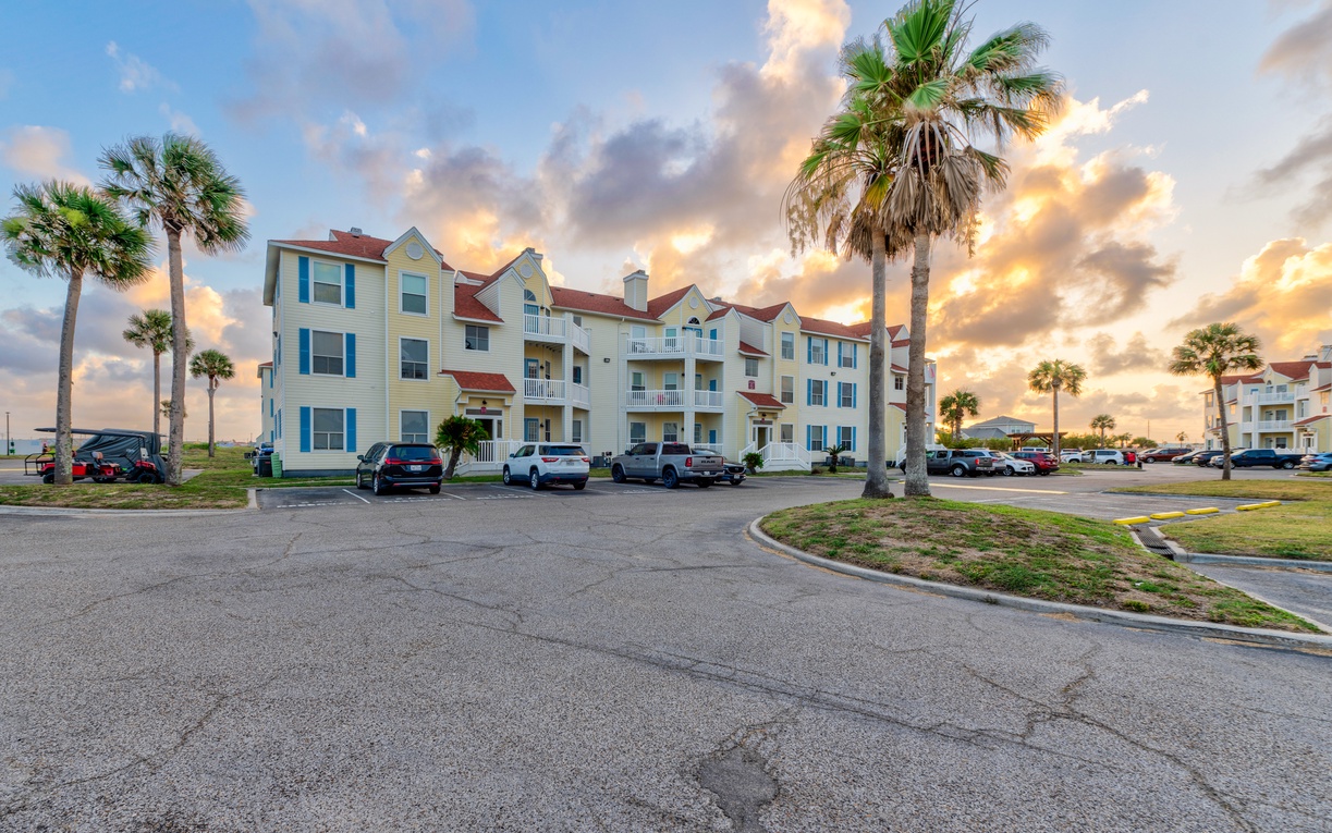 Multi-story coastal property building with red tile roofs set among tropical palms, offering convenient parking during golden hour.