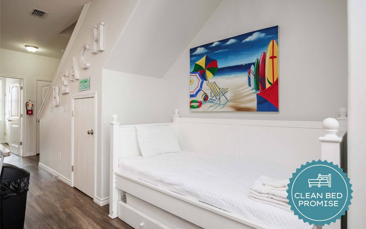 Relax in your bright loft bedroom featuring clean white linens, coastal artwork, and peaceful natural light streaming through the windows.
