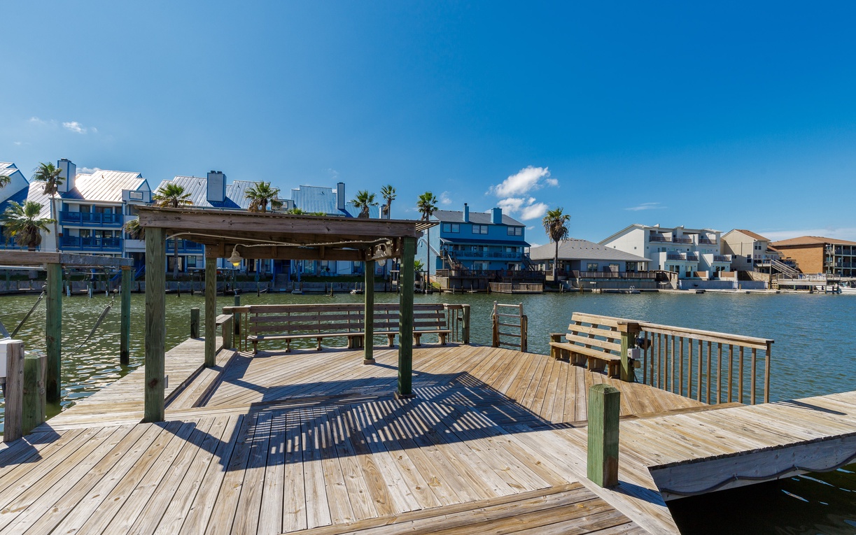 Waterfront dock with covered seating area overlooking calm waters and modern residential buildings.