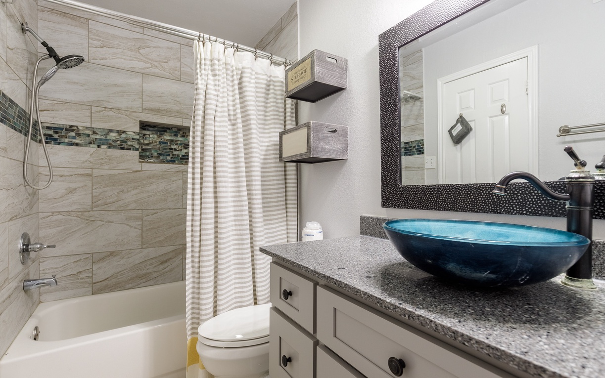 You'll love this modern bathroom featuring a stunning blue glass vessel sink, granite counters, and elegant tile work throughout.