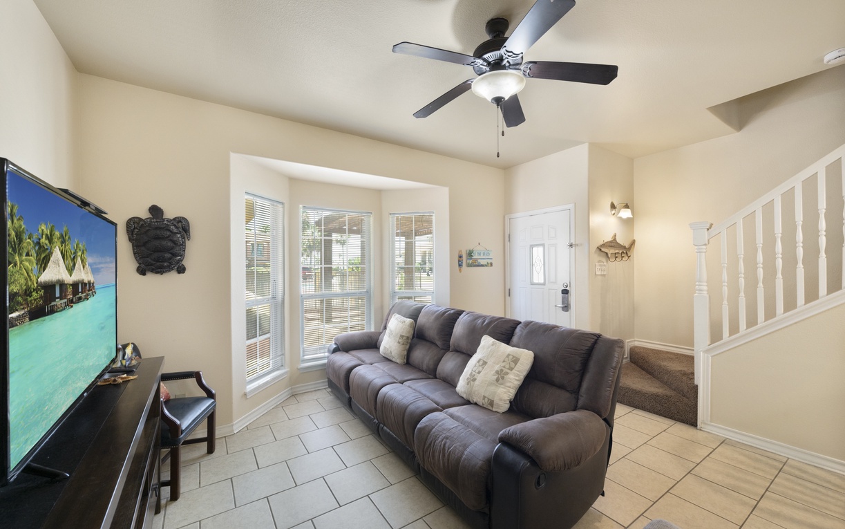 Settle into your cozy living space where a plush sofa invites relaxation beneath a gentle ceiling fan. Large windows flood the room with natural light, perfect for unwinding after beach adventures.