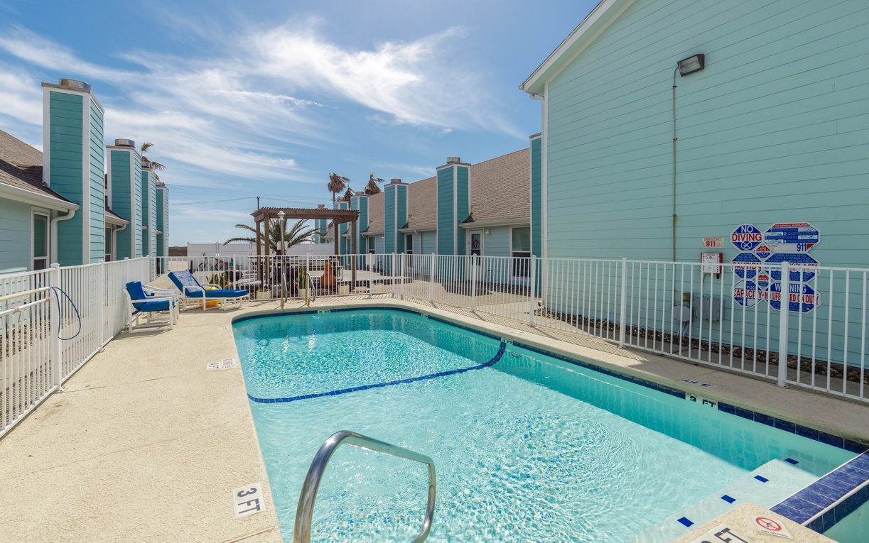 Sparkling pool surrounded by coastal buildings under blue skies with palm trees.