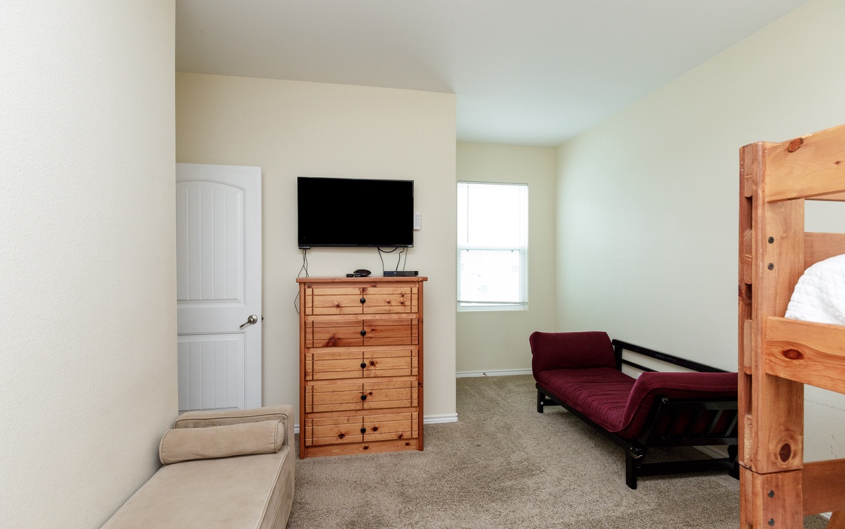 Unwind in this cozy bedroom featuring a wall-mounted TV, rustic wooden dresser, and comfortable seating perfect for relaxation.