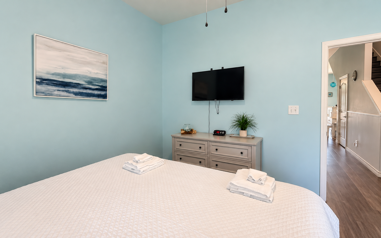 Unwind in your serene bedroom with calming coastal hues, crisp linens awaiting you, and modern comforts like a wall-mounted TV and charging station ready for your stay.