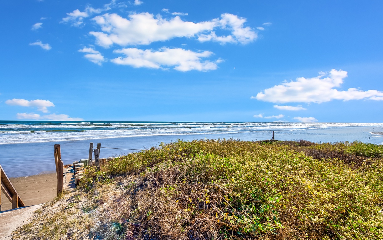 Pristine oceanfront location with direct beach access via wooden walkway, featuring rolling waves and endless coastal views.