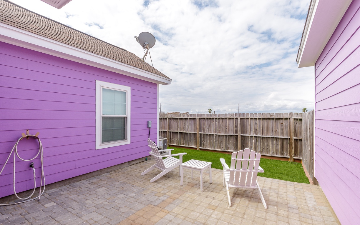Step into your private fenced backyard where vibrant purple walls create a cheerful atmosphere for relaxing on white patio furniture.