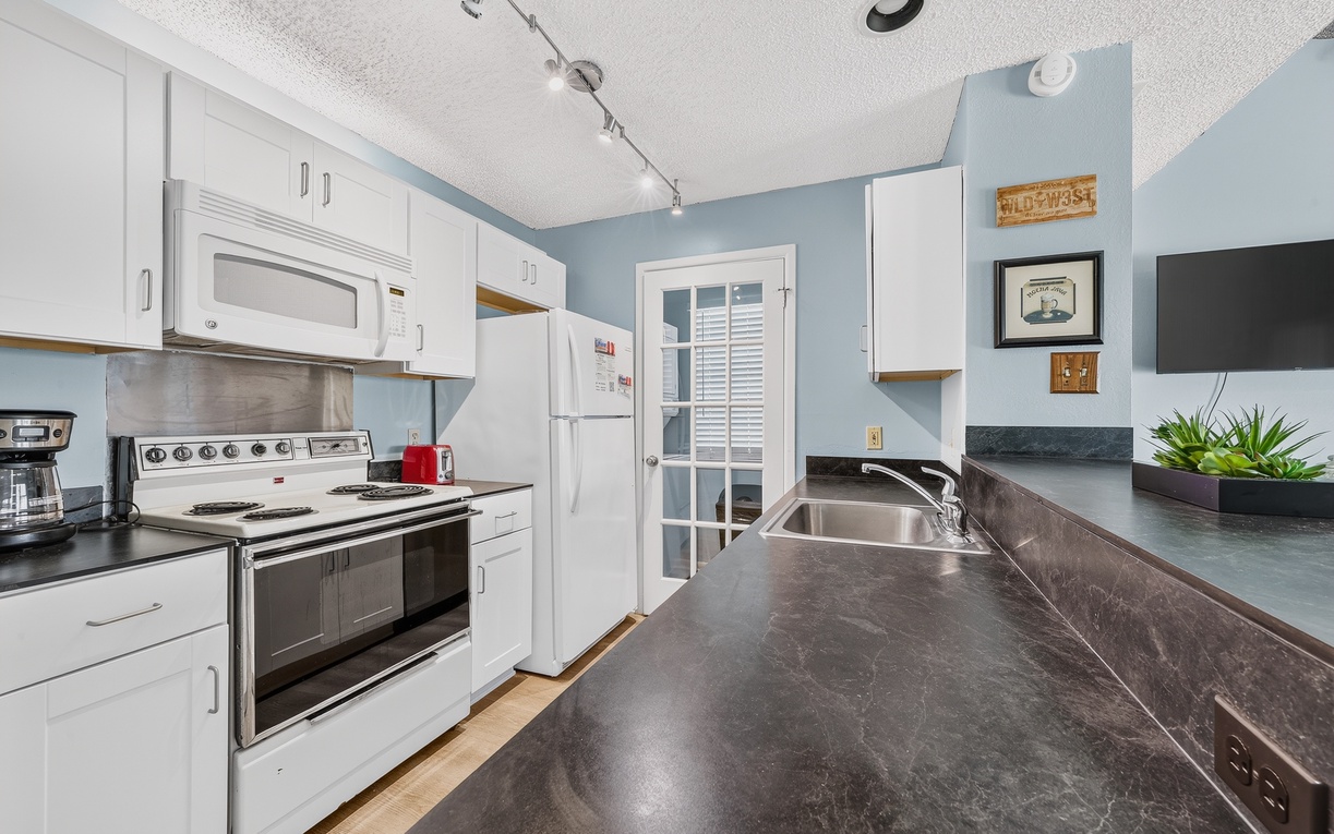 Prepare your favorite meals in this fully equipped kitchen featuring white cabinetry, spacious countertops, a full-size refrigerator, electric stove, microwave, and double sink for easy meal preparation and cleanup.