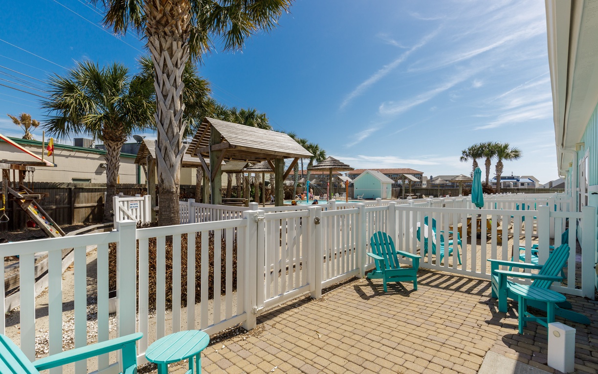 Your private patio features turquoise Adirondack chairs and tropical palms, creating the perfect coastal retreat for morning coffee or sunset relaxation.