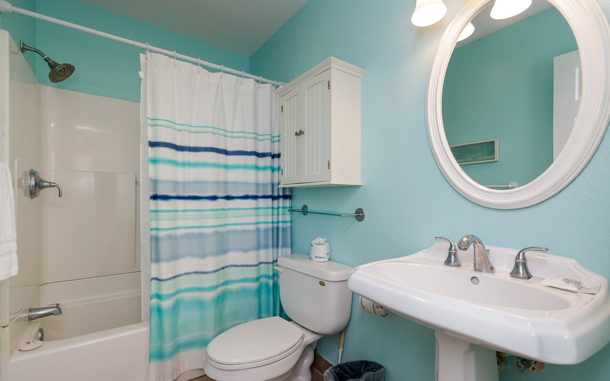 Your coastal-themed bathroom features soothing aqua walls, nautical striped shower curtain, and bright lighting for refreshing starts to beach days.