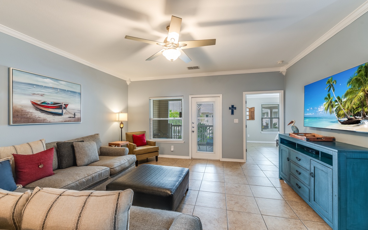 Sink into plush seating while the ceiling fan keeps you cool in this coastal-themed living room with beach artwork and tropical vibes.