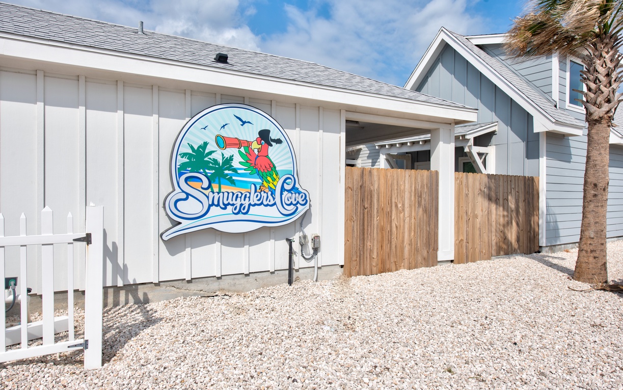 Charming coastal property entrance featuring the colorful 'Smugglers Cove' sign, complete with tropical flamingo design and palm tree details.