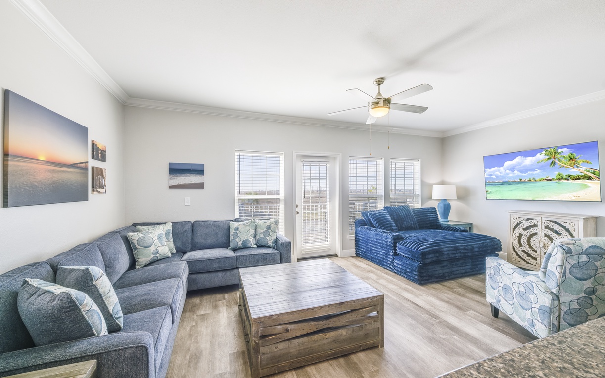 Relax in your spacious living room with comfortable sectional seating, coastal artwork, and French doors opening to your private outdoor space.