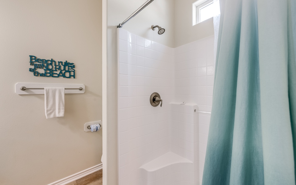 Step into your fresh, bright bathroom with a spacious shower perfect for washing away sandy adventures.