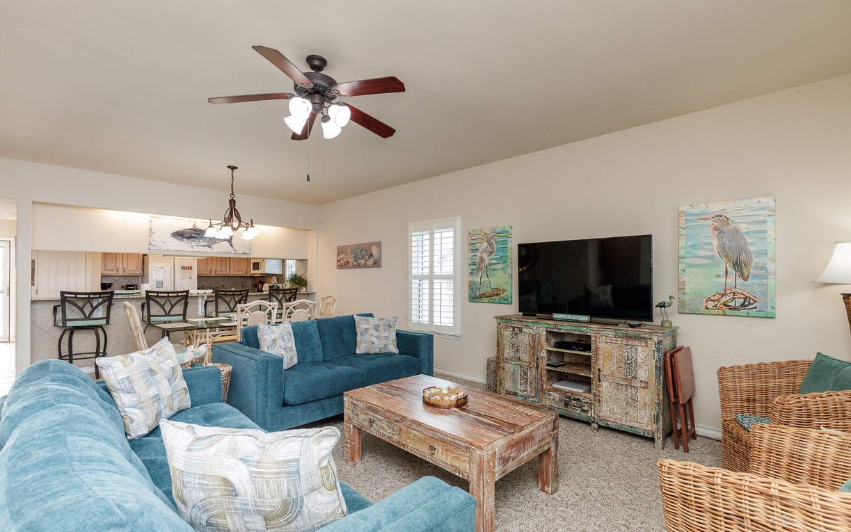 Relax in your coastal living room with comfortable blue sofas, charming beach décor, and ceiling fan for your perfect getaway.