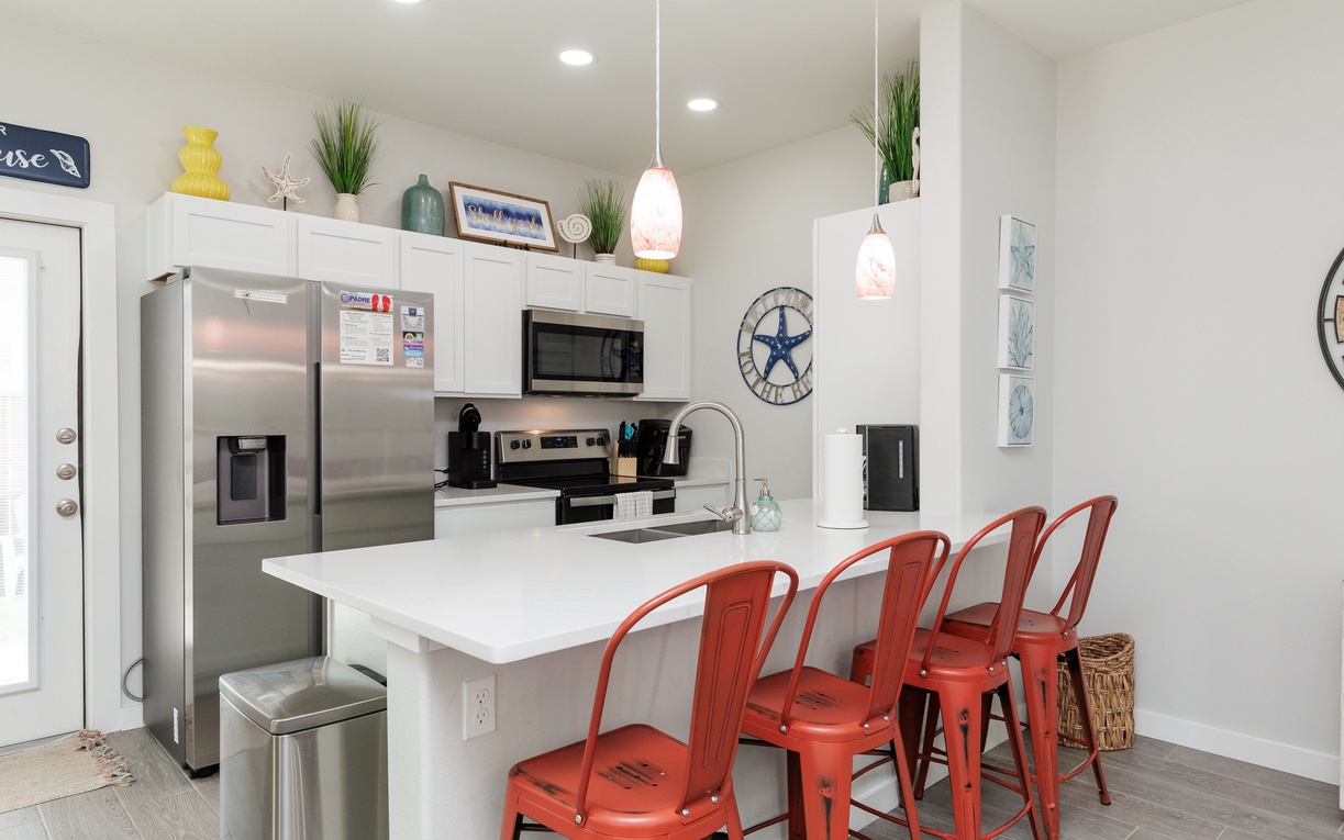 Gather around your stylish breakfast bar with vibrant coral stools while enjoying modern appliances and coastal-inspired décor that makes cooking together a joy.