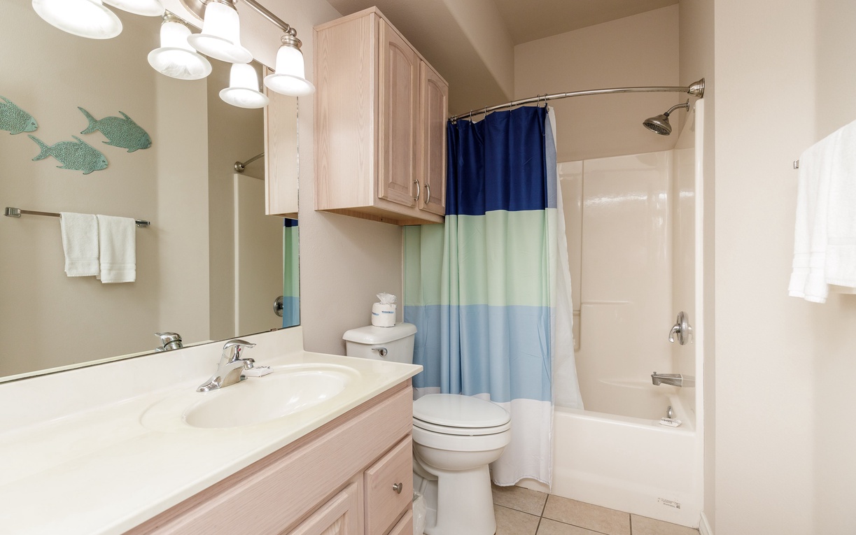 Your coastal-themed bathroom features a spacious tub-shower combo, vanity storage, and charming ocean wall decals for a refreshing seaside feel.