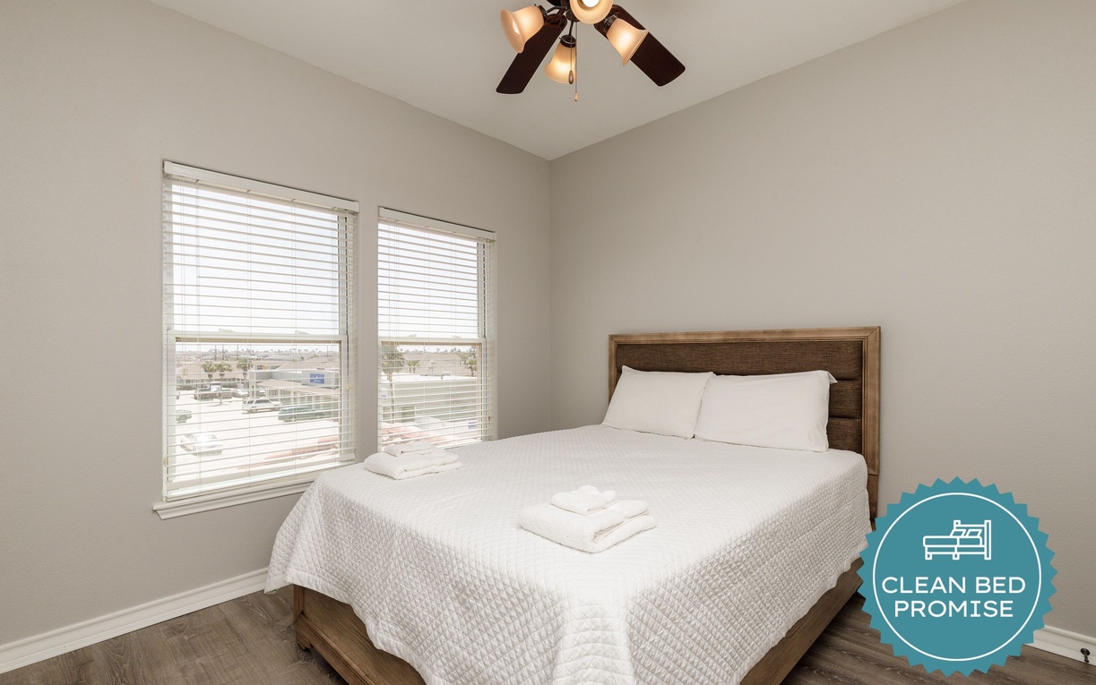 Your comfortable bedroom features crisp white linens and a warm wooden headboard, with peaceful views through dual windows.