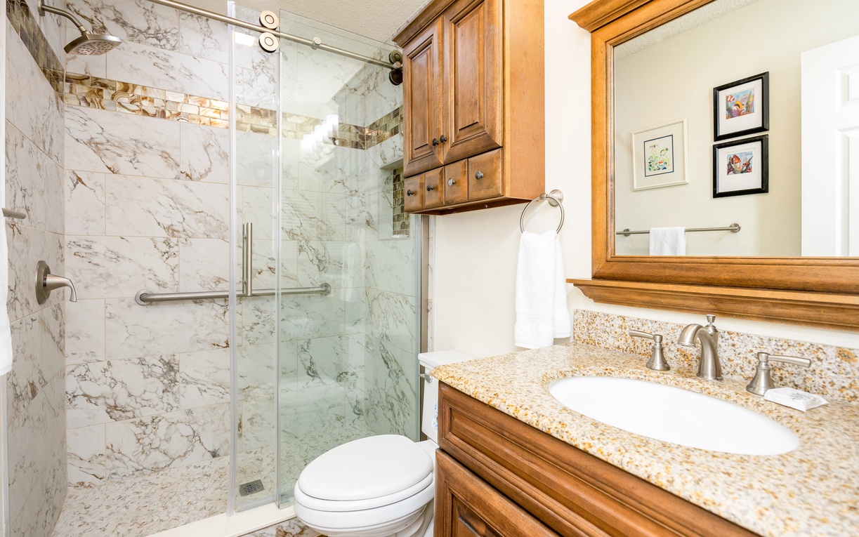 Indulge in your private marble sanctuary with elegant granite countertops, rich wood cabinetry, and a spacious glass shower.