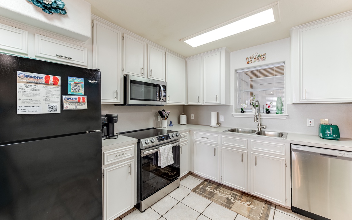 Your fully equipped kitchen features bright white cabinetry, stainless steel appliances, and natural light from the skylight above.