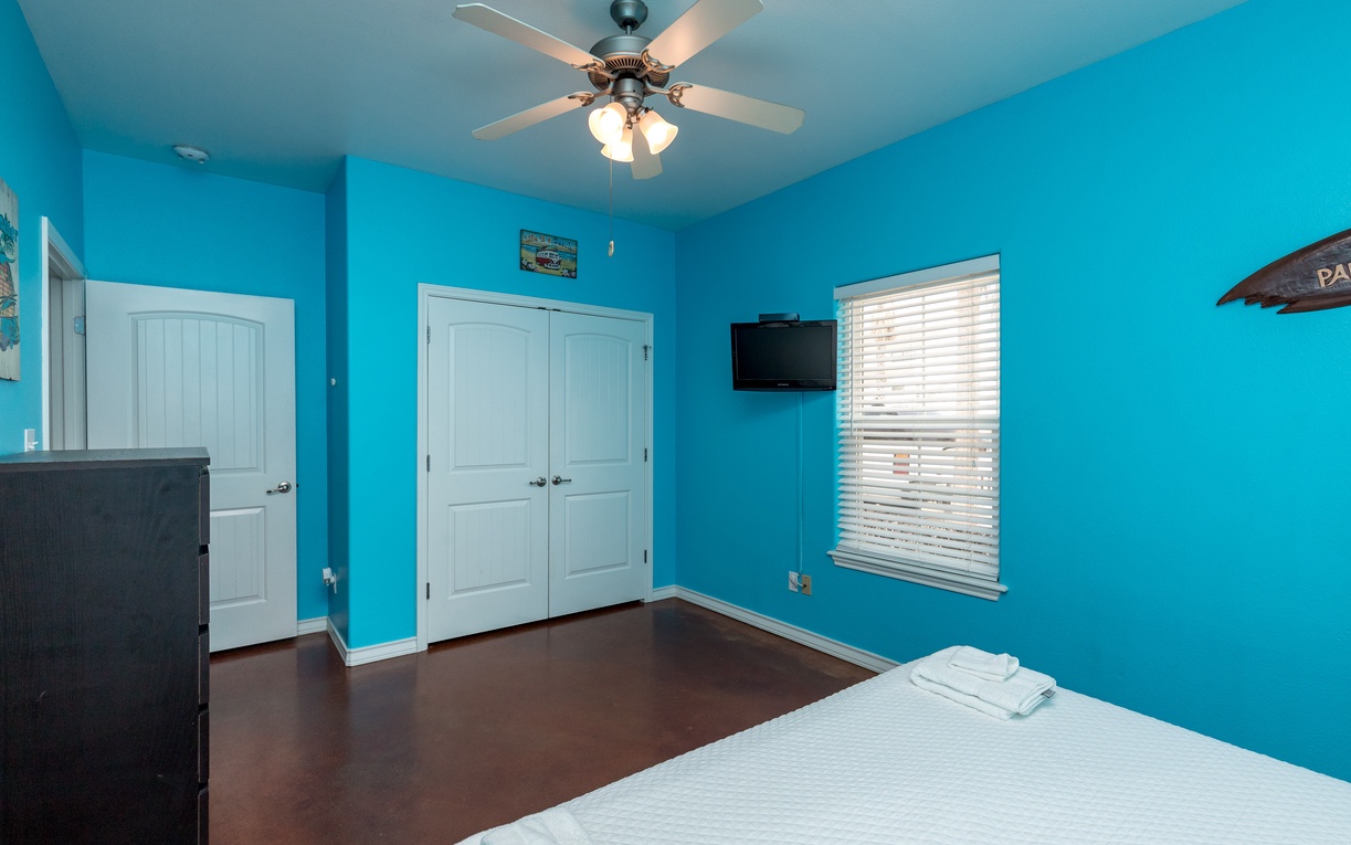 Drift off in your bright, cheerful bedroom with vibrant turquoise walls, cozy linens, and a gentle ceiling fan overhead.