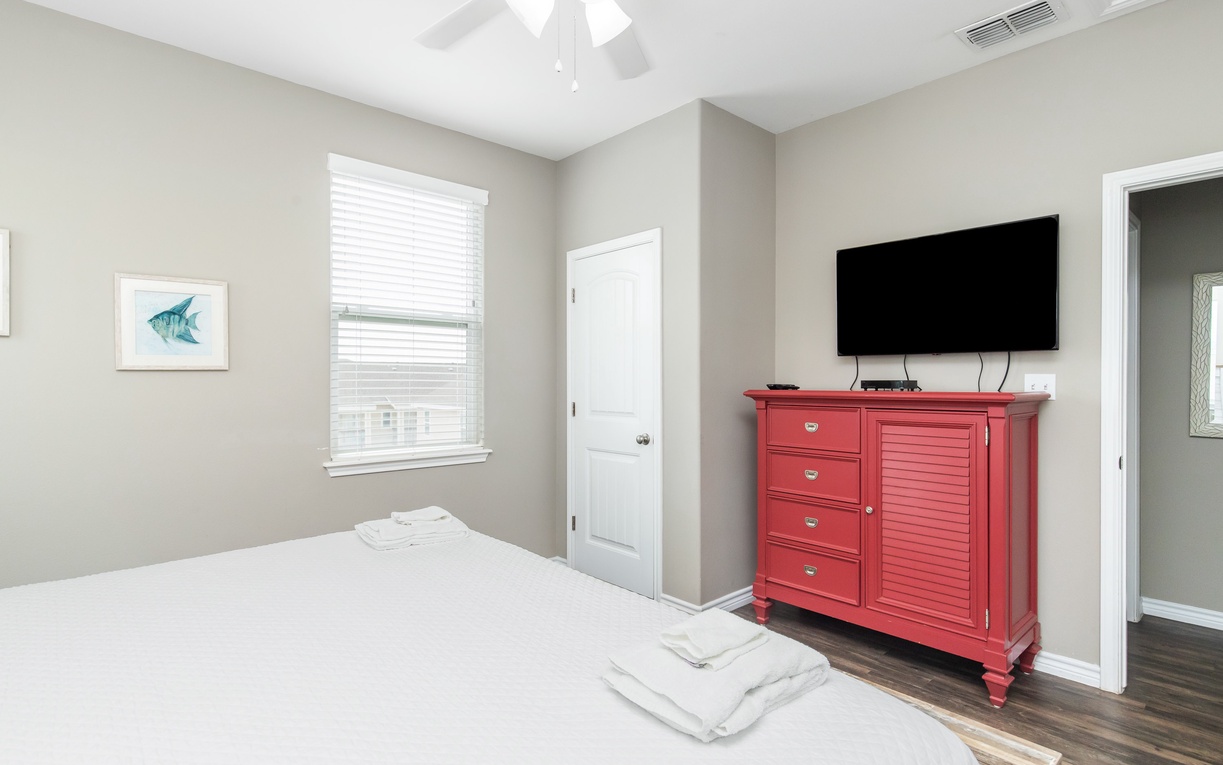 Relax in your bright, airy bedroom featuring a comfy bed, coastal artwork, and entertainment center with flat-screen TV.