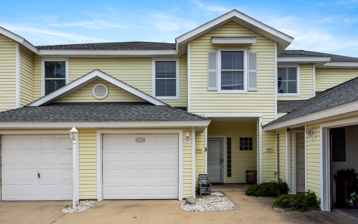 Bright yellow townhouse with attached garage and covered entry creates a welcoming arrival experience in this residential community.