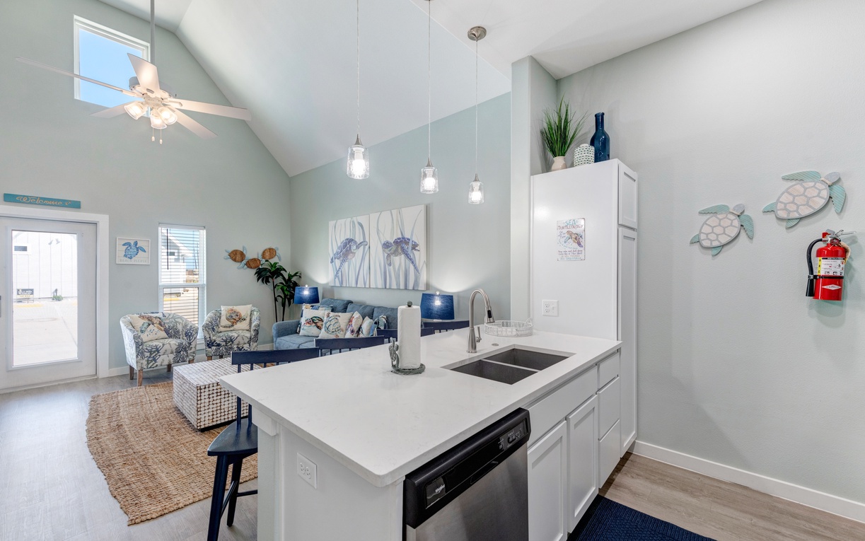 Your bright, open kitchen flows seamlessly into the coastal-themed living space, featuring modern appliances and charming sea turtle wall art.