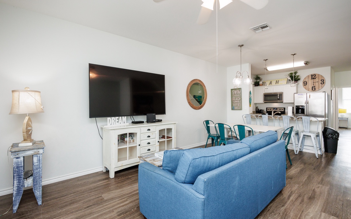 Relax in your bright living space with comfy blue seating, large TV, and open kitchen - perfect for memorable vacation moments.