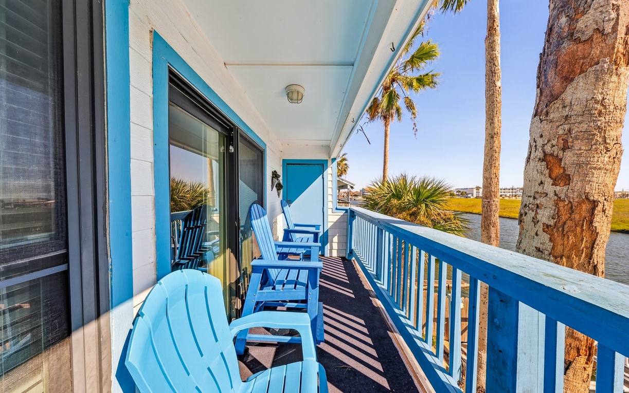 Kick back in vibrant Adirondack chairs on your private waterfront balcony, where swaying palms frame peaceful views of the water and coastal marshlands beyond.