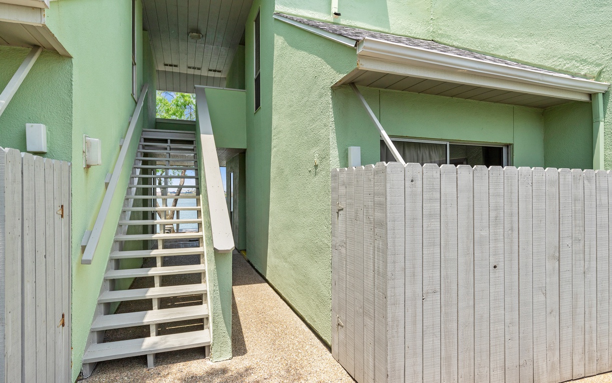 Charming green building exterior with wooden staircase leading to upper level accommodations and private fenced courtyard area.