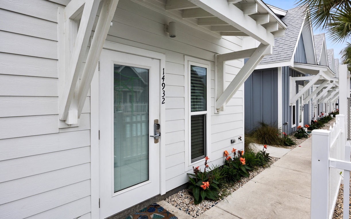 Clean white cottage entrance with bright tropical flowers and covered entry provides a welcoming arrival to your coastal retreat.