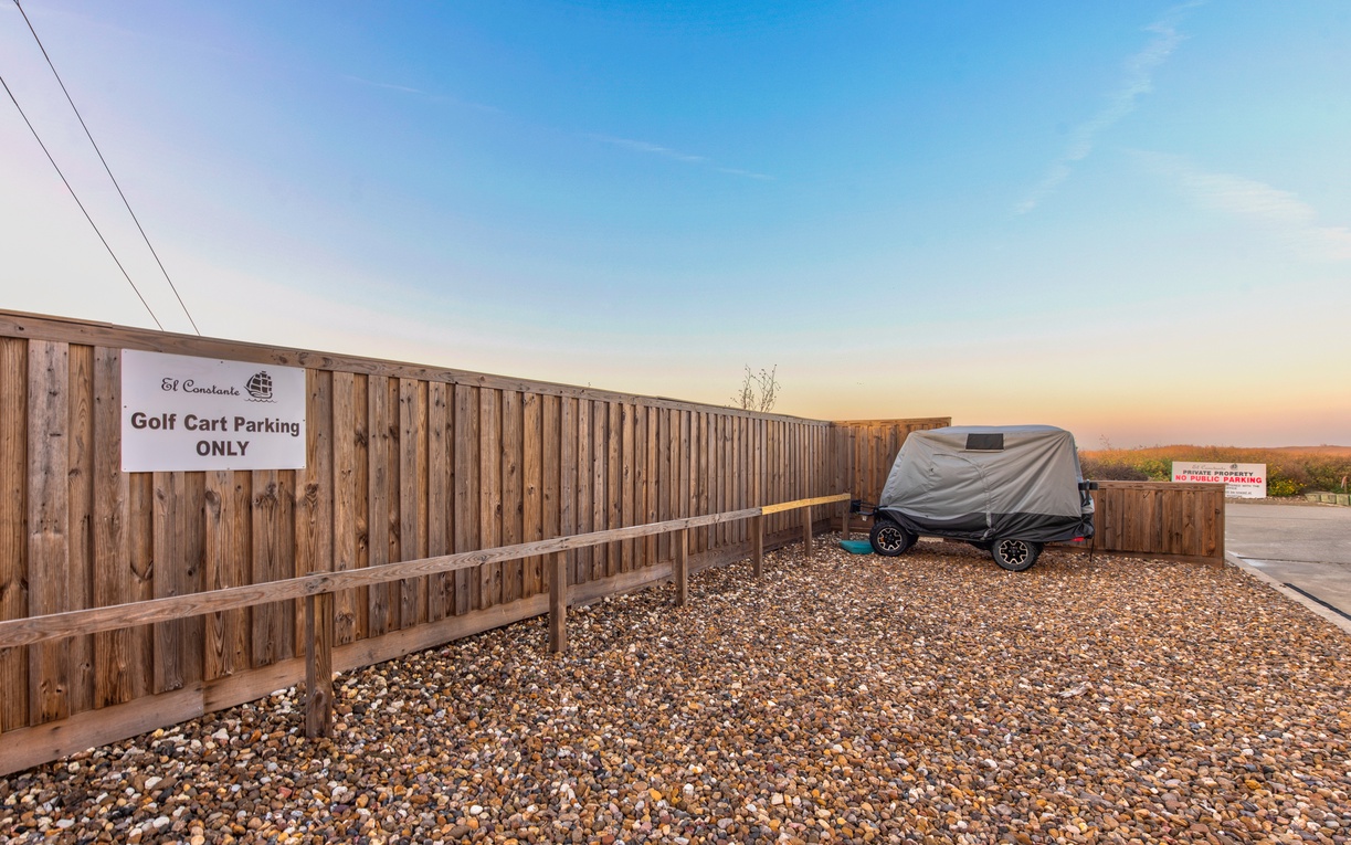 Dedicated golf cart parking area with gravel surface and wooden fencing at sunset.