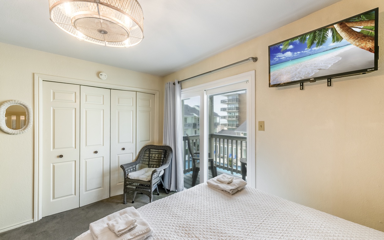 Unwind in your bright bedroom featuring a ceiling fan, tropical TV, cozy wicker chair, and balcony doors that welcome natural light.