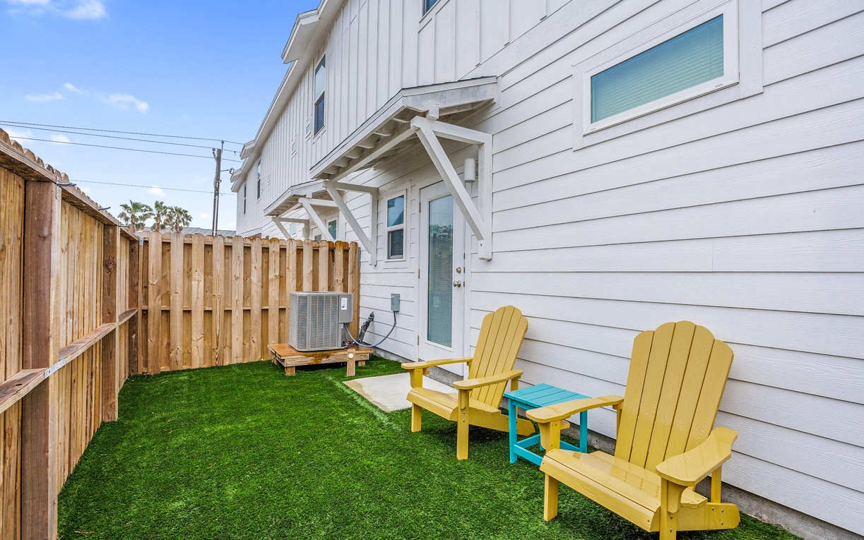 Your private backyard oasis awaits with cheerful yellow Adirondack chairs and a turquoise side table on lush green turf—perfect for morning coffee or evening relaxation.