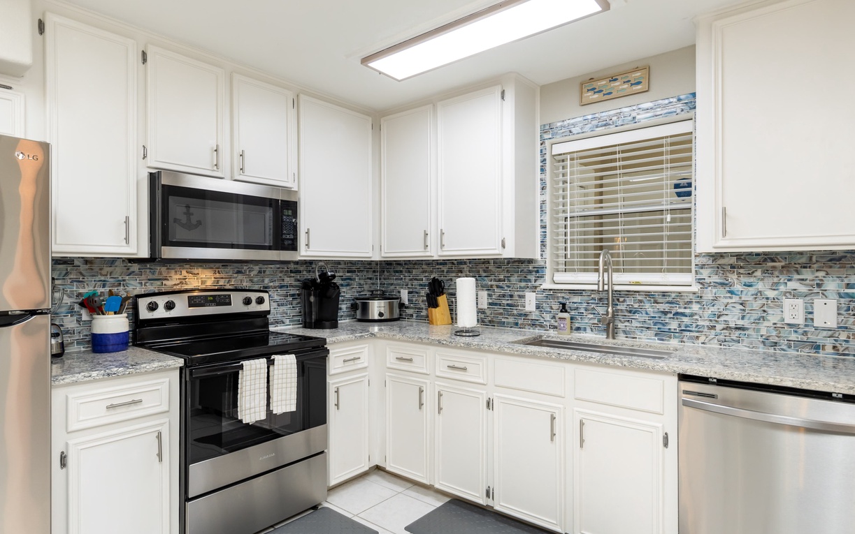 Your fully equipped kitchen awaits with granite counters, stainless appliances, and coastal-inspired tile backsplash—perfect for preparing meals.