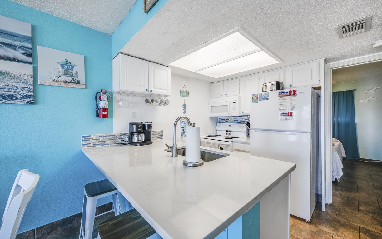 Picture yourself brewing morning coffee in your bright, beach-themed kitchen. White counters, stainless appliances, and coastal blue walls create a cheerful space for preparing meals during your stay.