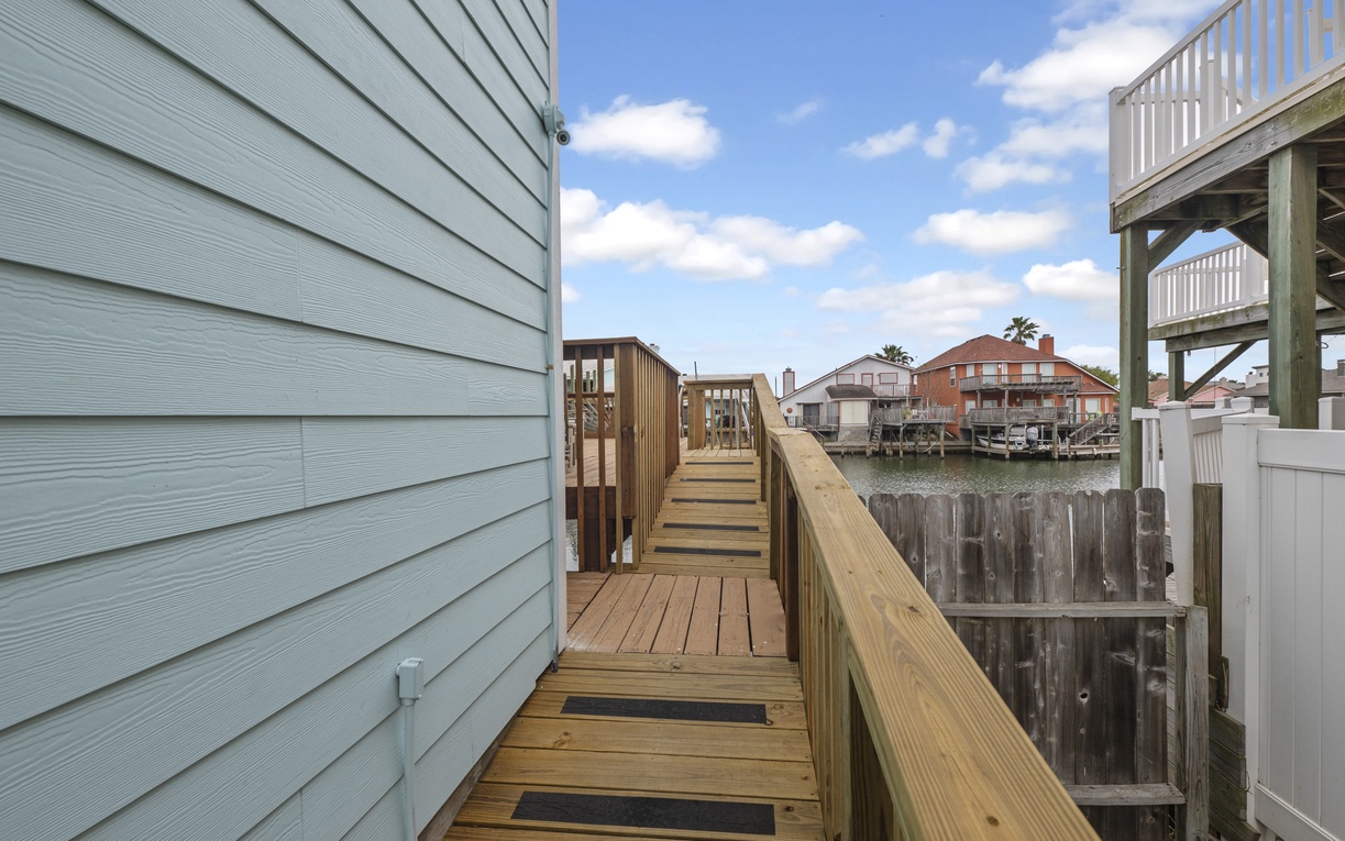 Wooden walkway connecting waterfront property to neighboring homes with canal views.