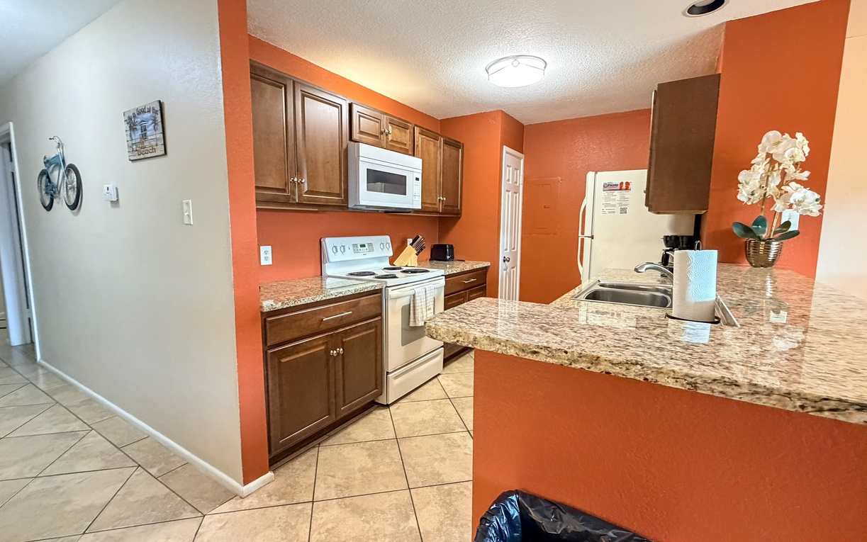 Cook your favorite meals in this fully equipped kitchen with granite counters, stainless appliances, and warm orange accents.