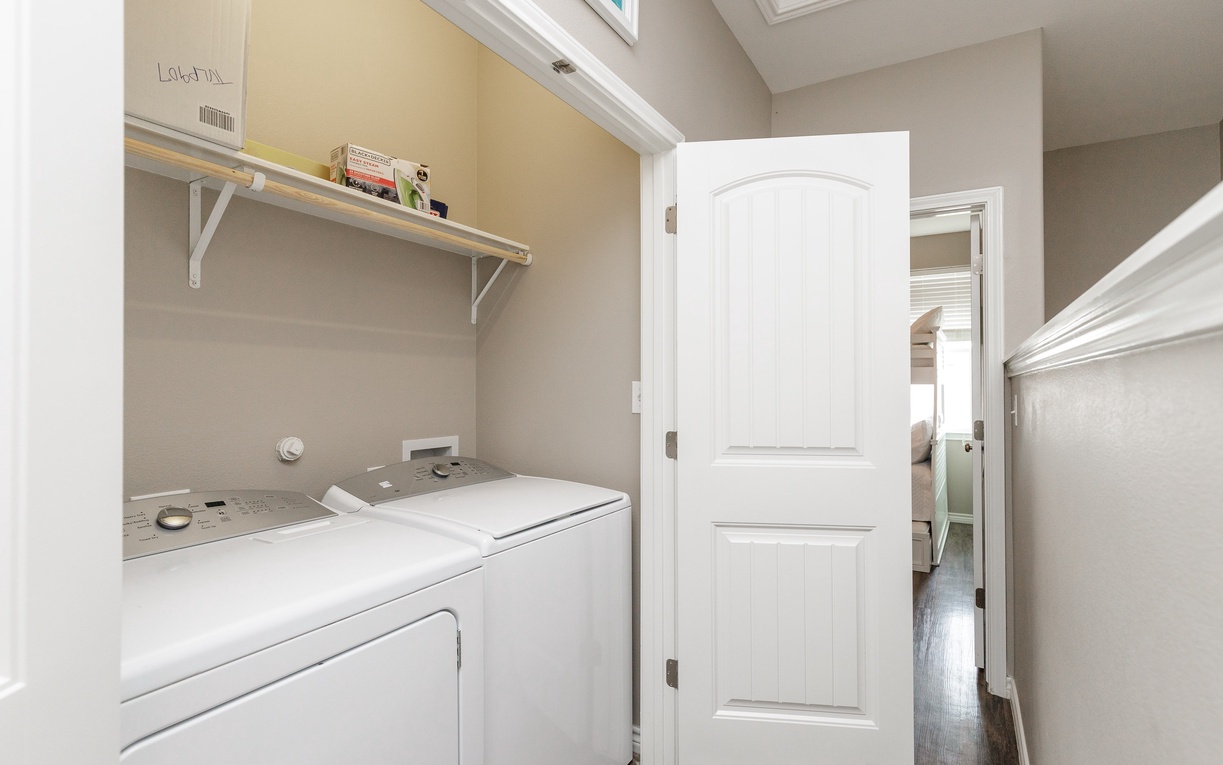 Keep your wardrobe fresh with this convenient in-home laundry room, featuring a full-size washer and dryer with helpful storage shelving above.