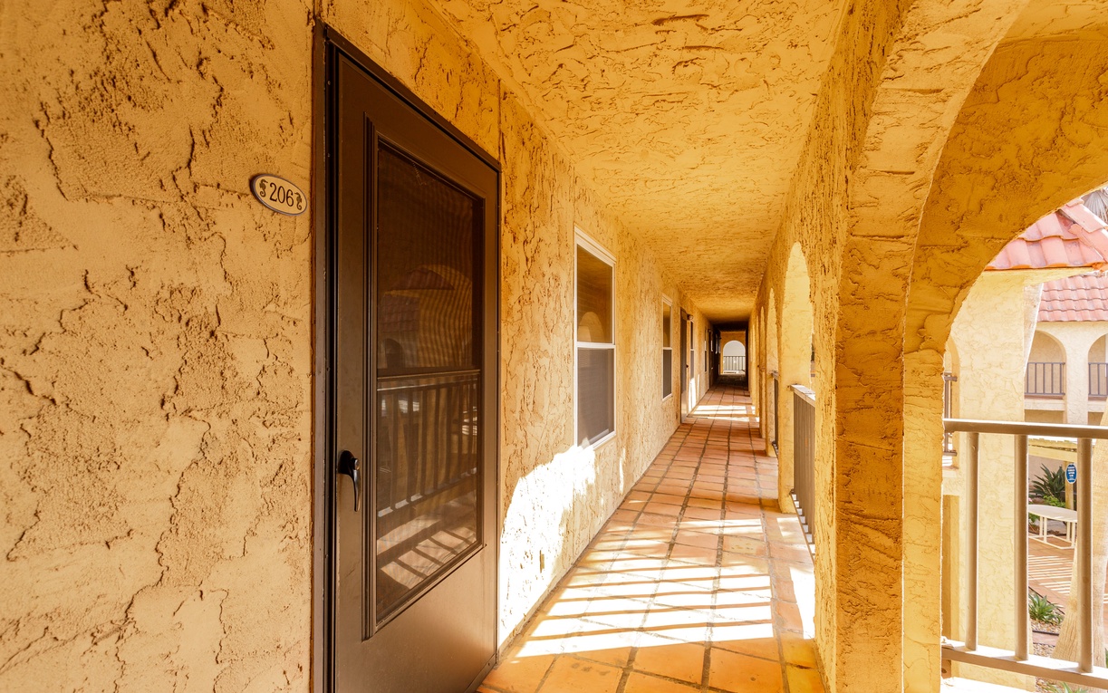 Step onto your private covered balcony where golden sunlight creates beautiful patterns across terracotta tiles, offering peaceful views of the surrounding architecture.