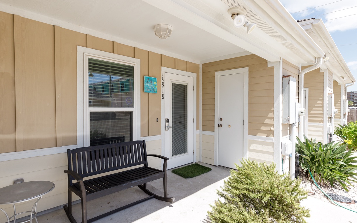 Step onto your covered patio where a cozy bench invites you to relax with morning coffee surrounded by lush greenery.