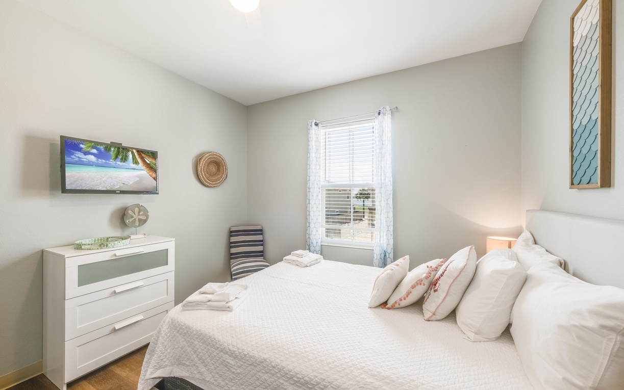 Your serene bedroom awaits with coastal artwork, soft linens, and natural light streaming through the window for peaceful mornings.