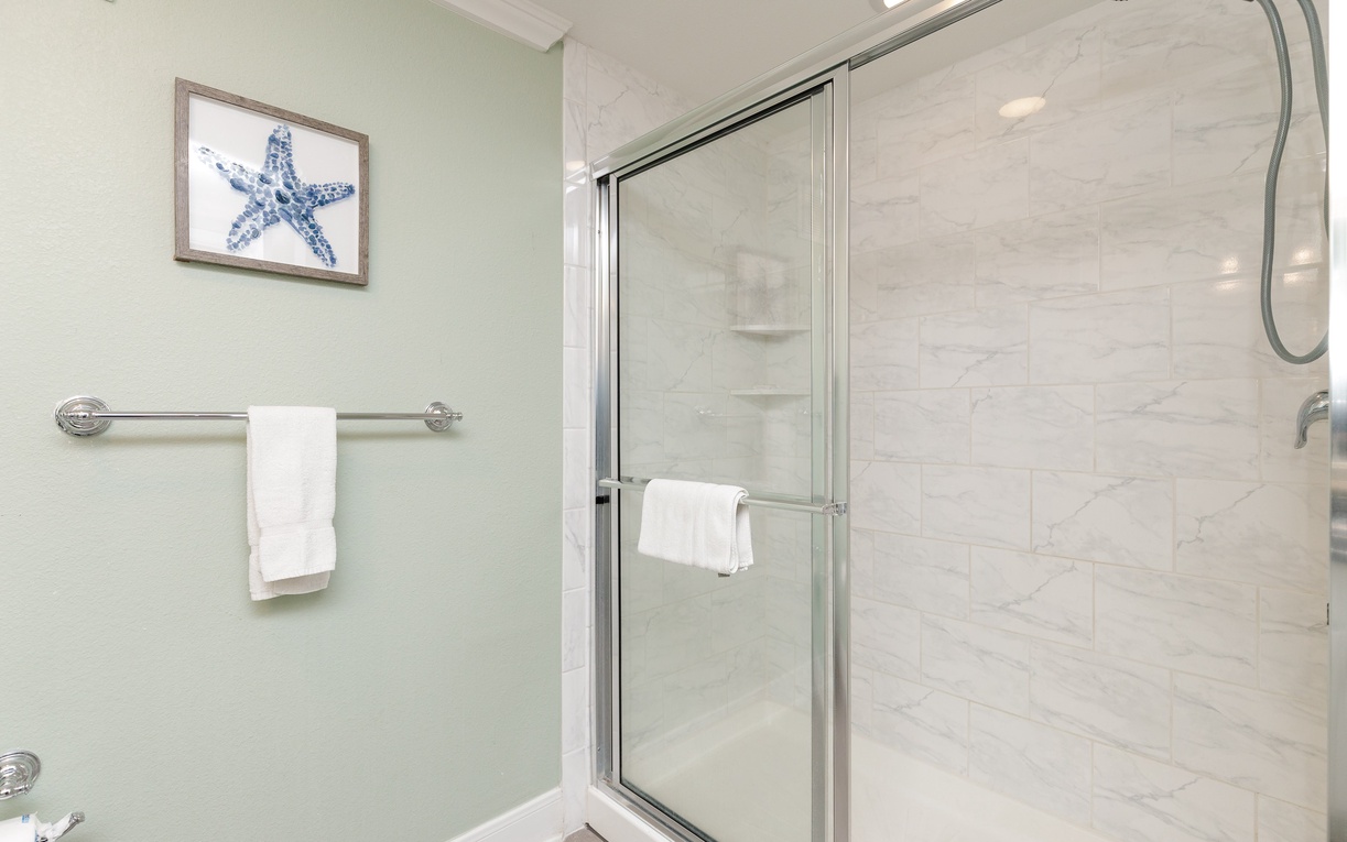 Step into your spa-like bathroom with a spacious glass-enclosed shower, marble-look tiles, and charming coastal décor that makes every morning feel refreshing.