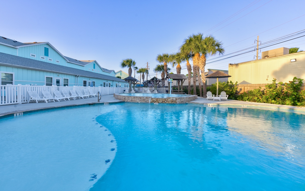 Spacious swimming pool with tropical palms and colorful coastal buildings creating a vibrant resort atmosphere.